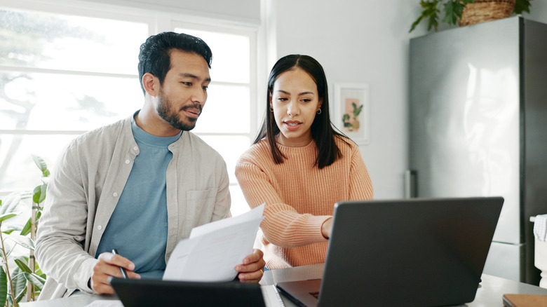 Couple looking over their insurance paperwork sitting in front of a laptop in their kitchen