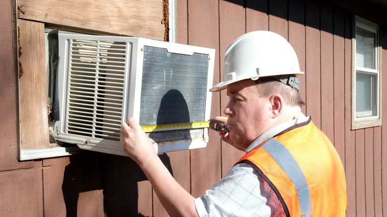 A worker measuring a window air-conditioner