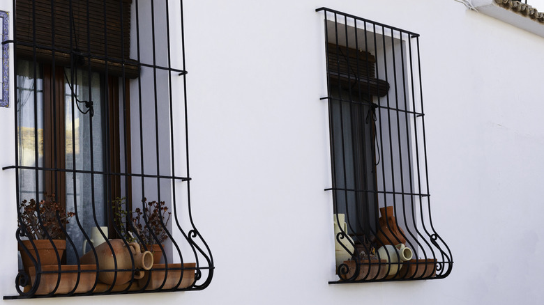 Two windows covered with iron potbellied window bars with clay pots on the sills