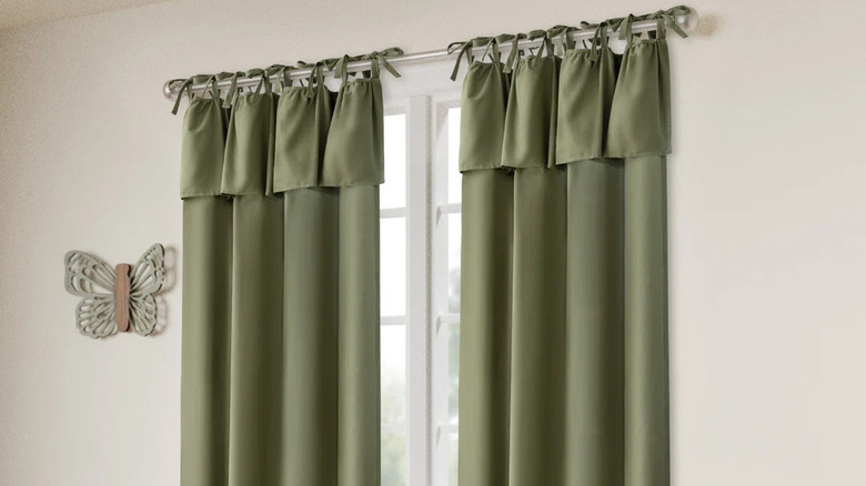 Green tie top curtains in front of a window on a silver rod