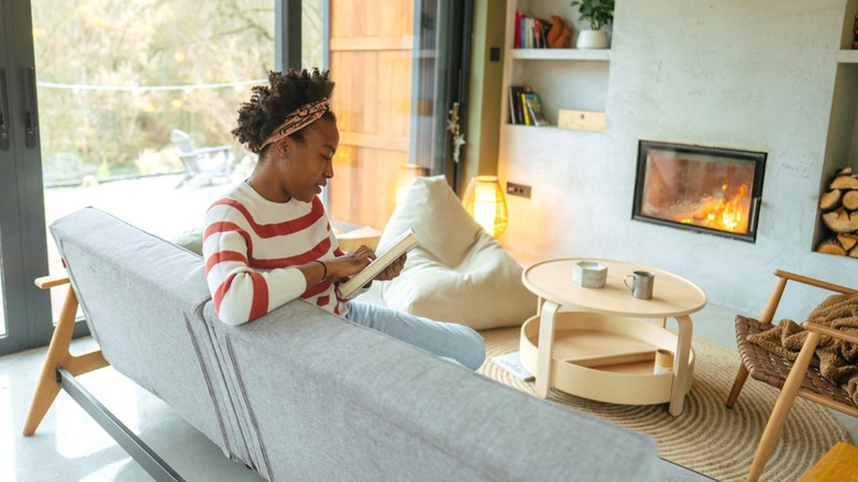Woman reading while sitting on couch in front of fireplace in living room.