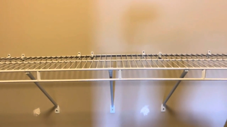 An empty wire closet shelf with extra loop clips an an additional support arm installed to stop it bowing.