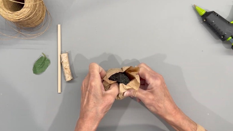 A person folding a paper bag around a piece of pool noodle to create a rustic pumpkin decoration.