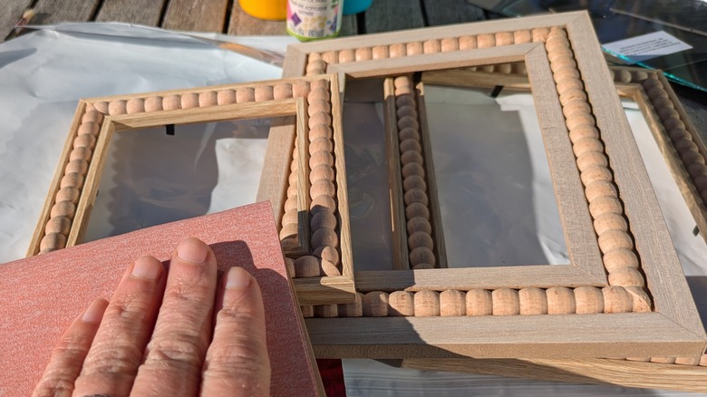 A hand rubs Dollar Tree wooden picture frames with sandpaper.