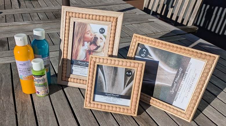 Dollar Tree wooden bead frames standing next to Dollar Tree paints on an outdoor table