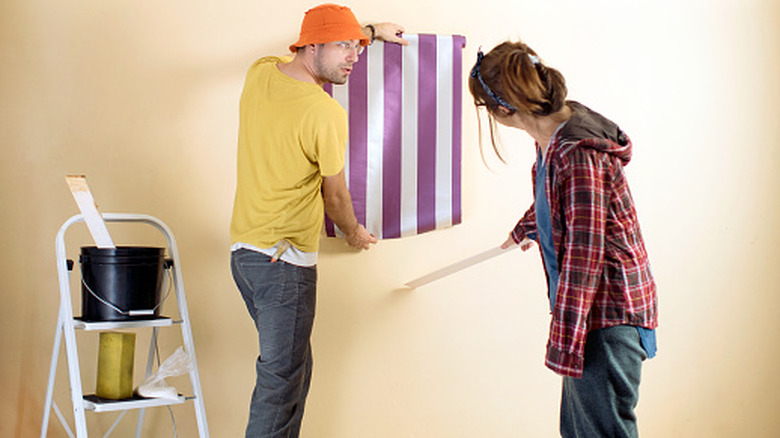 A man and a woman are finalizing the wallpaper for a wall