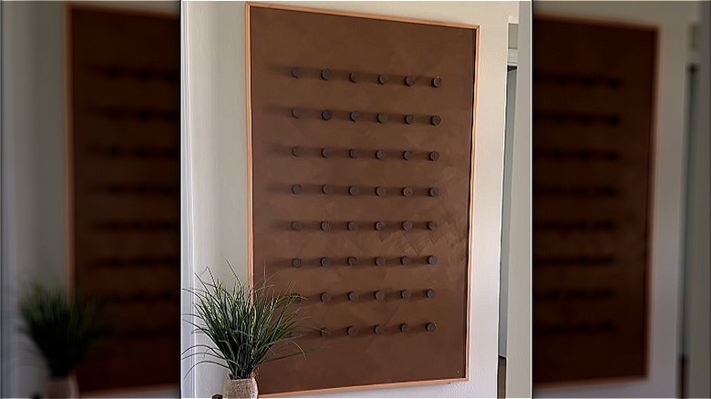 A large, elegant wall art hung up on a large wall, with a potted plant next to it