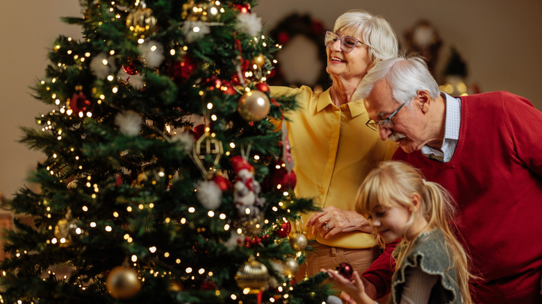Grandparents hanging ornaments on tree with grandchild