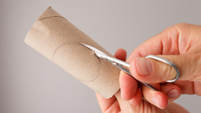 a hand is using nail scissors to cut through a toilet paper roll.