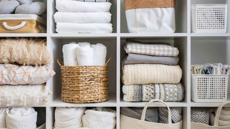 Organized linen closet in white and tan with folded towels, baskets, and bins