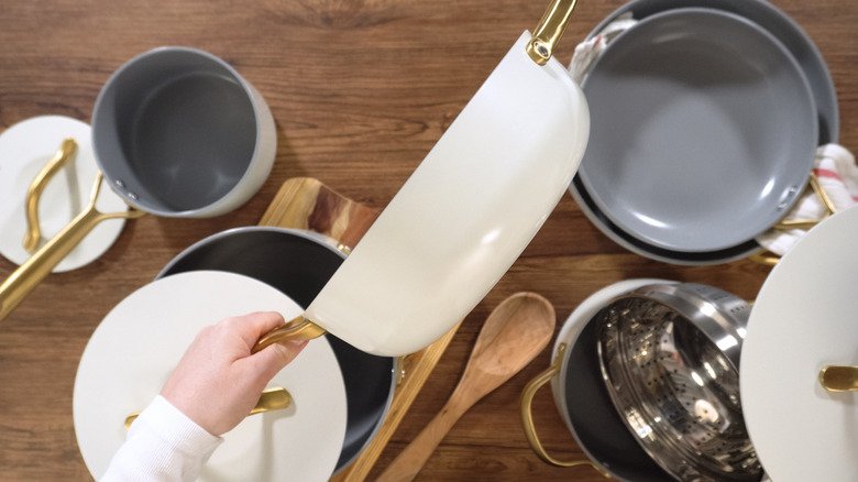 Person holding a white pot above a matching cookware collection sitting on a countetop