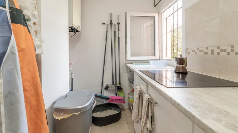 small room with cleaning supplies and brooms piled up against the wall