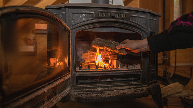 Person putting a log on a burning flame in a wood-burning stove