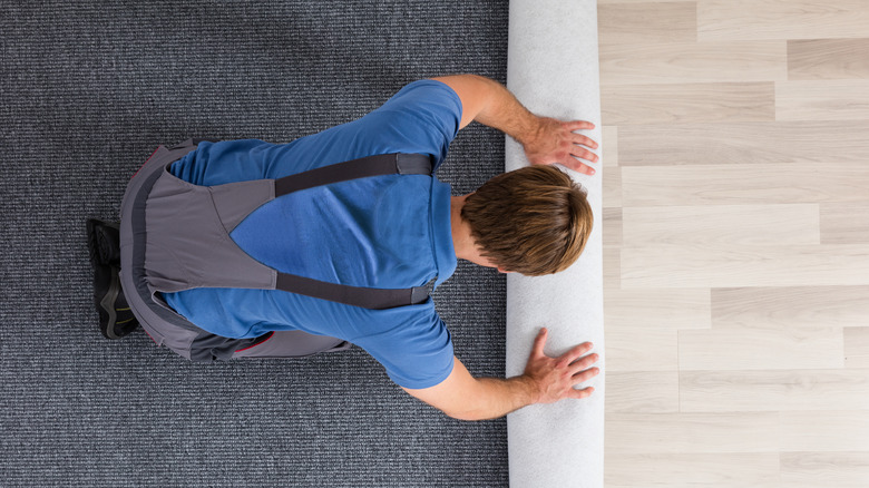 Man rolling carpet over wood floor