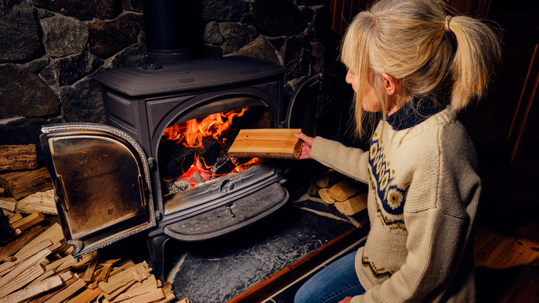 Woman puts log in wood stove