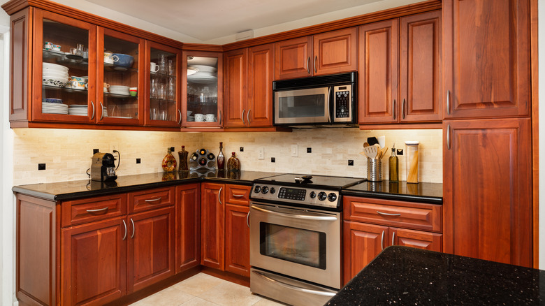 A dated kitchen with red cherry wood cabinets and stainless steel appliances.