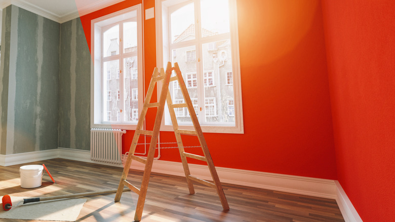 A home with empty, patched walls that change to a reddish orange where the light hits it with a ladder in the front