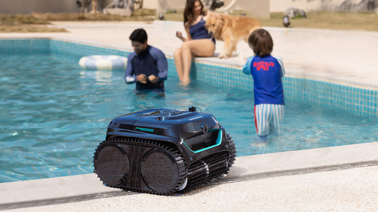 A WYBOT C2 on the edge of a pool with a family in the background