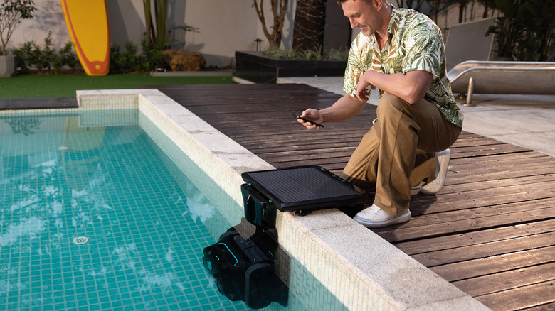A man kneeling by the pool and controlling a WYBOT S2 Solar with his phone