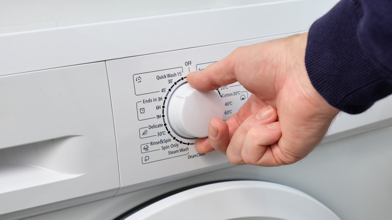 A person adjusting the temperature setting on their washing machine