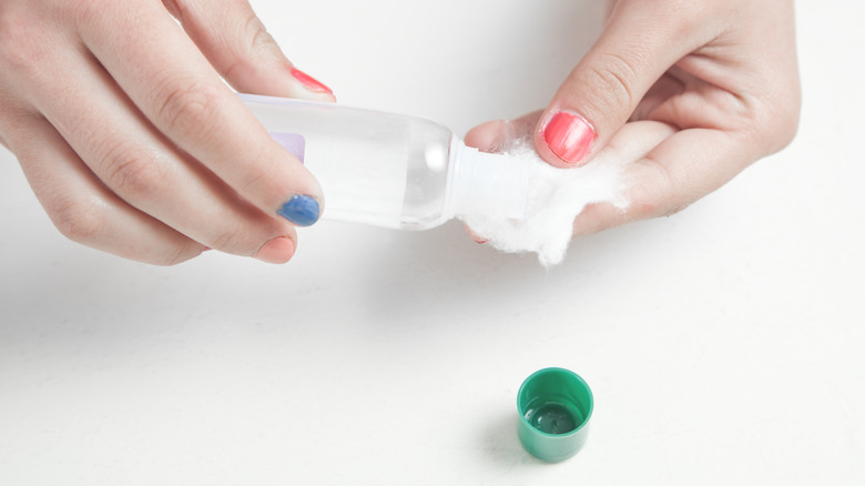 A person dampening a cotton ball with acetone