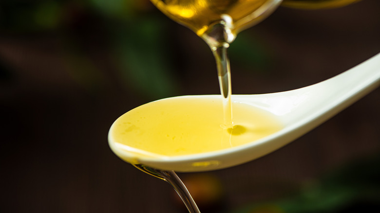 A person pouring olive oil into a white spoon