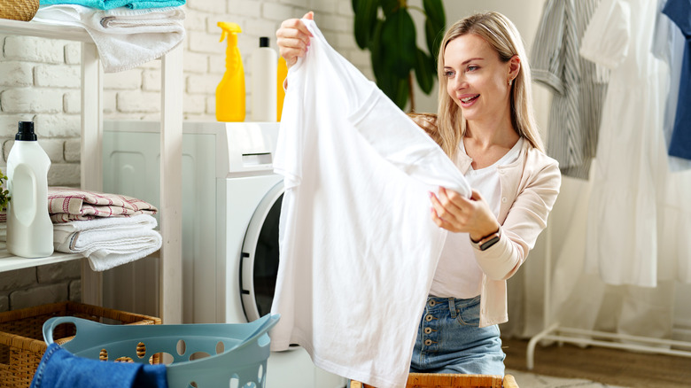 woman holding up a white tee shirt in a laundry room