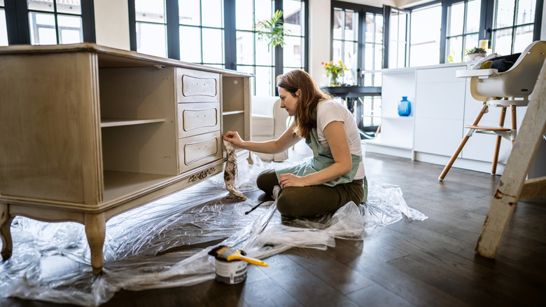 A person painting a wooden dresser