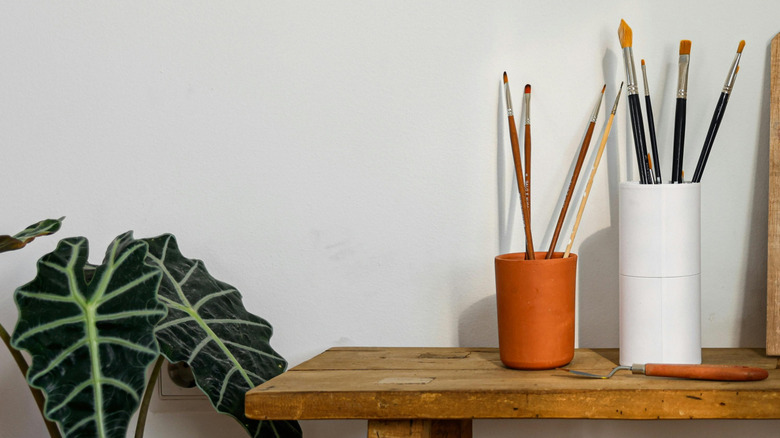 Paintbrushes in cups beside plant