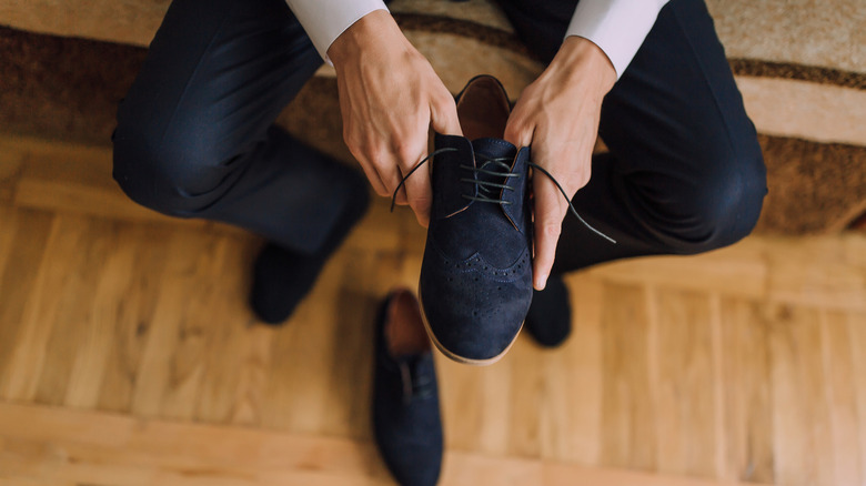 A man putting on a pair of black suede shoes