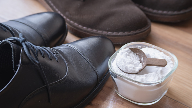 A small cup of baking soda next to two pairs of work shoes