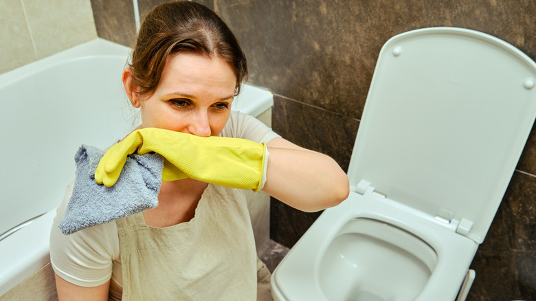 person covering nose cleaning toilet