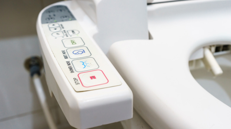 A toilet with a bidet control panel on the side