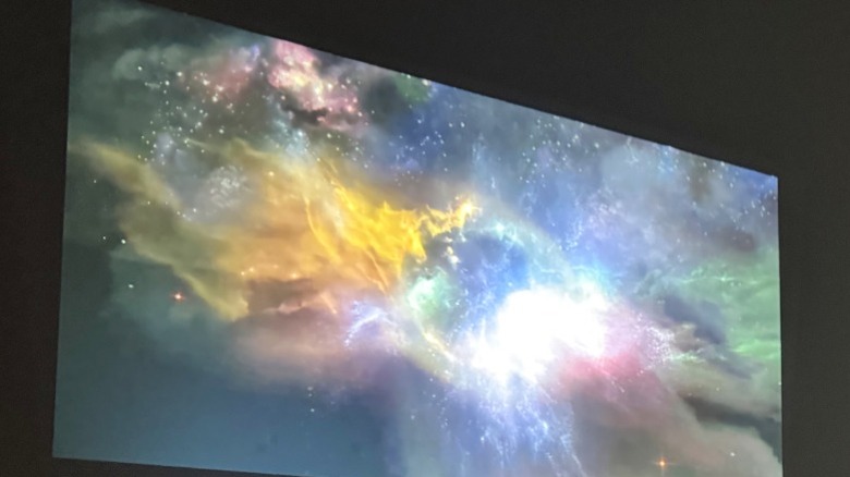 Yarber L2 Plus projecting cosmic screensaver on wall while sitting on multi-colored area rug