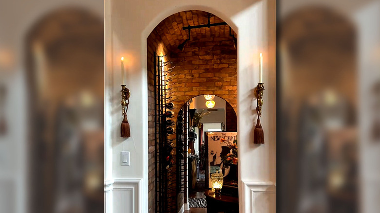 Tassekls hanging from candle sconces in an arched walkway toward a wine cellar