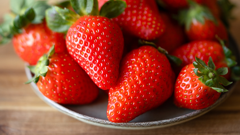 Shallow bowl of strawberries pictured up close.