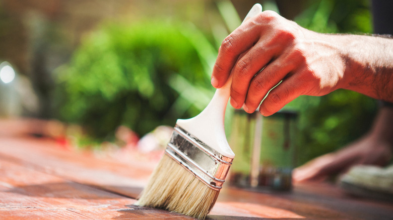 A hand holding a brush while refinishing a deck.