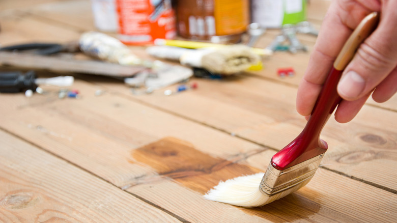 A man's hand holds a brush covered in stain or sealant and passes it over the board of a wood deck.