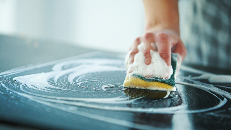 Person uses too much soap while cleaning their black countertop.