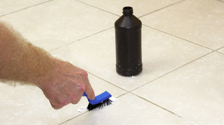 A person scrubbing dirty grout with hydrogen peroxide and baking soda paste