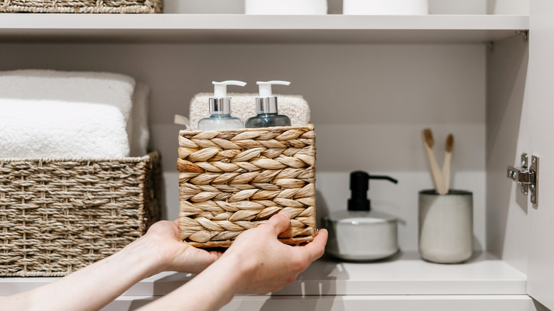 Person putting a storage basket filled with bathroom supplies on a shelf