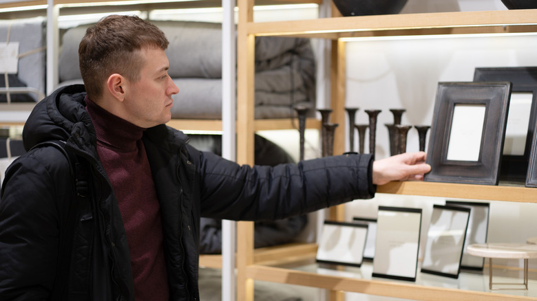 A man examines a picture frame on the shelf at a home decor store.