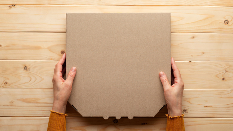 Person holding pizza box over wooden surface