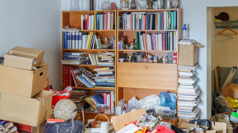 Piles of stuff in front of a bookcase full of books.