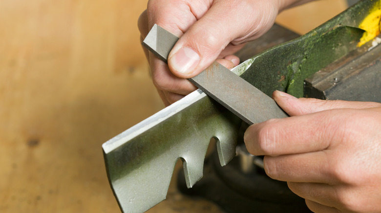 person using metal file for lawn mower blade