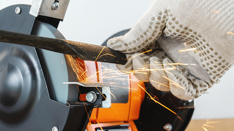 person sharpening lawn mower blade with sharpener