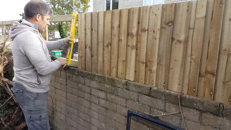 a man builds a wooden picket fence on top of a retaining wall
