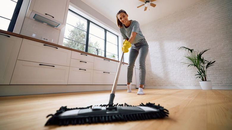 Woman smiling as she mops a laminate or wood floor with a microfiber mop