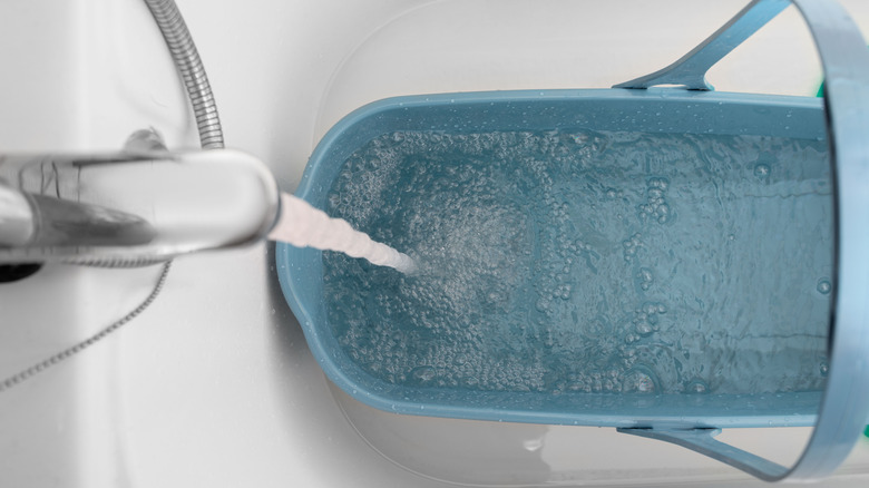 Clean water flows from a bath faucet into a blue bucket with a handle