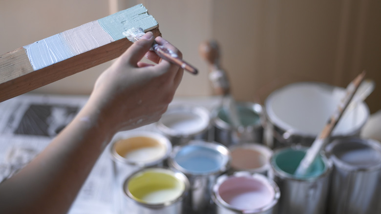 Person testing paint colors on plank of wood